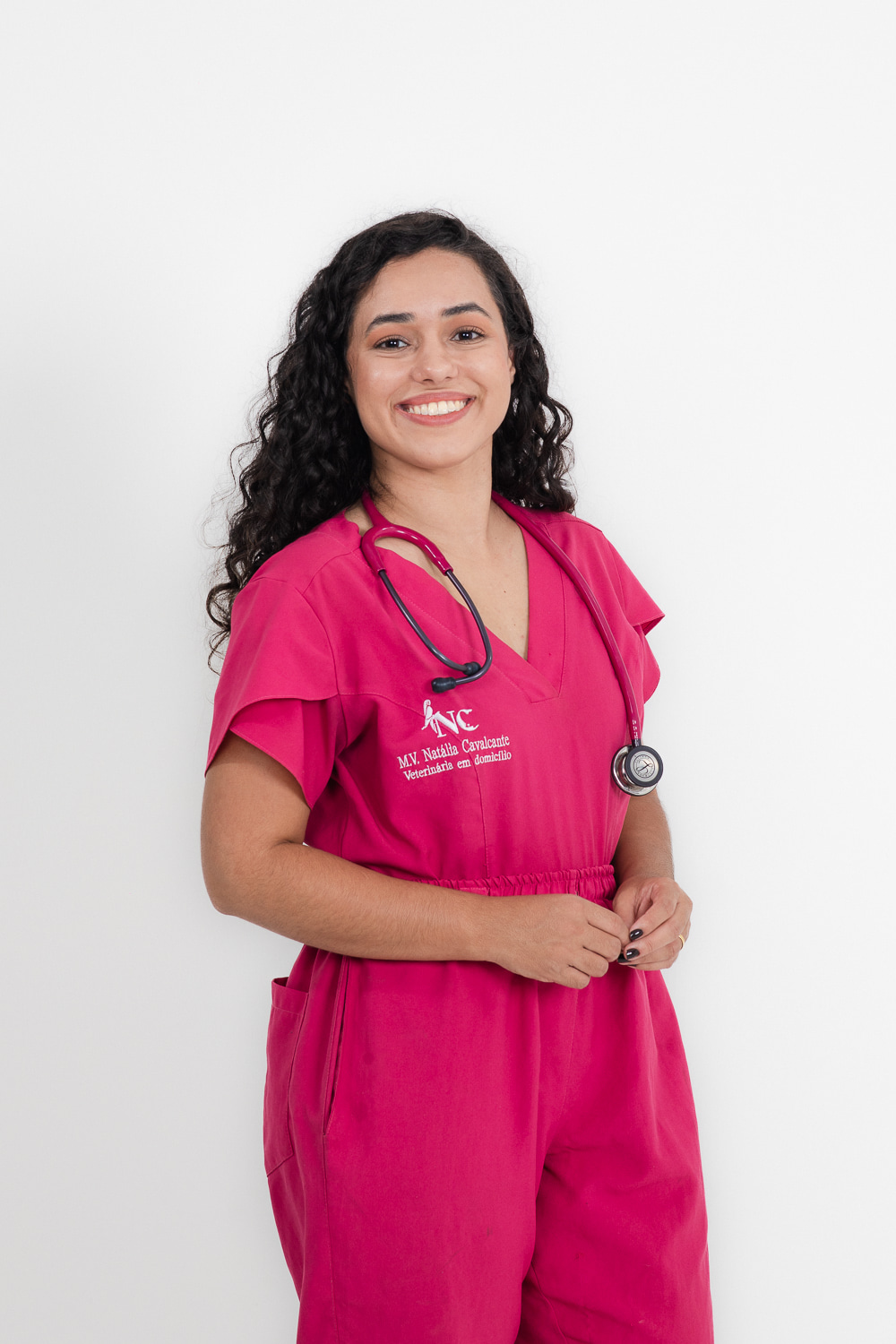 Dra. Natália Cavalcante sorrindo com estetoscópio, vestindo scrub rosa